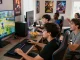 กลุ่มเพื่อนร่วมสนุกเล่นเกม playme8 ในห้องนั่งเล่นทันสมัย มีหน้าจอใหญ่แสดงตัวละครเกม
